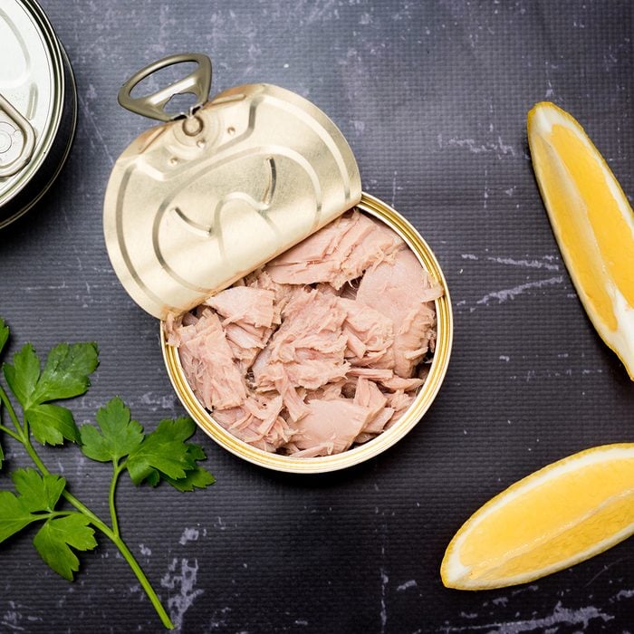 Opened tuna can with parsley and lemon slices on a black cutting board.