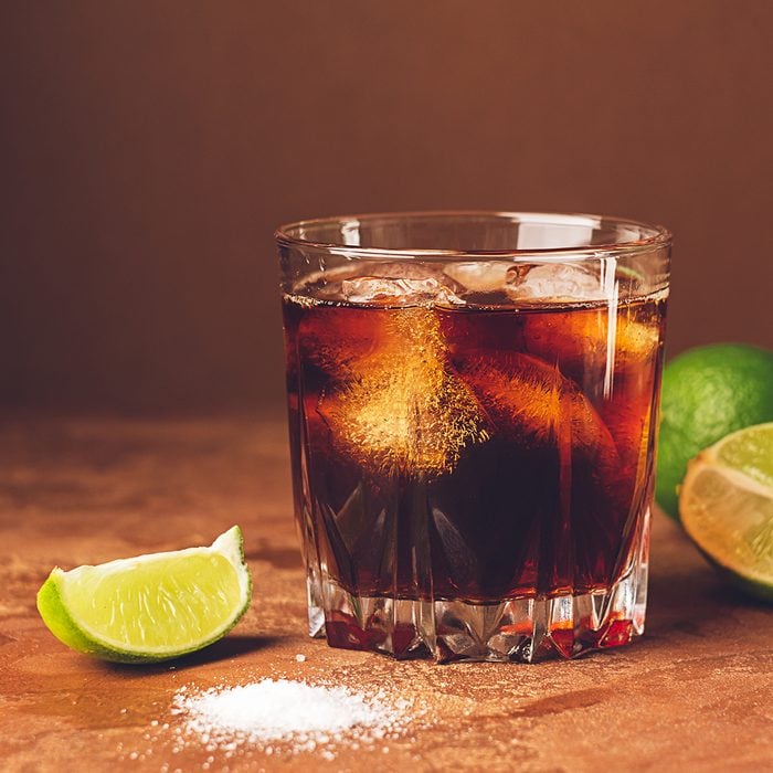 Cold cocktail drink with ice and pieces of juicy lime in a glass on a dark brown background.