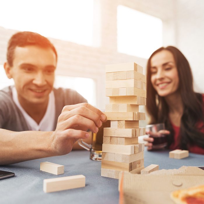 The company of young people plays a table game called jenga. 