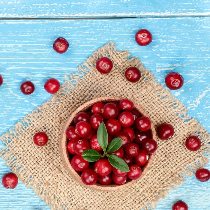 Cranberry with leaf in bowl on blue wooden background