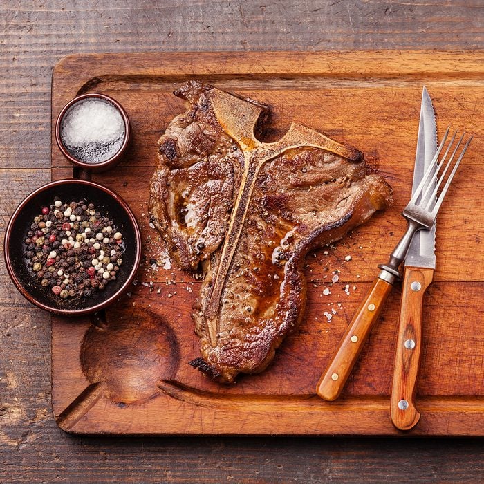 Grilled T-Bone Steak with salt and pepper on meat cutting board on dark wooden background