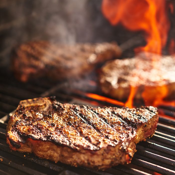 steaks cooking over flaming grill