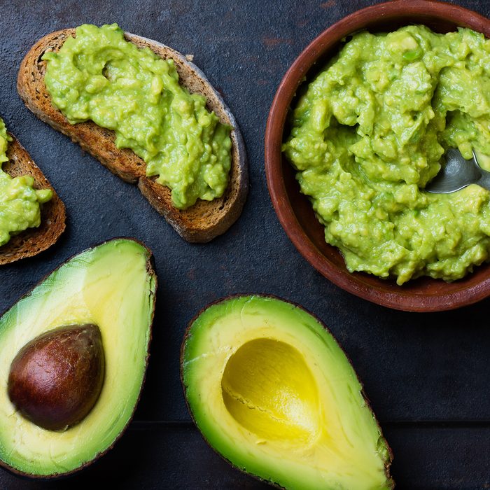 Traditional latinamerican mexican sauce guacamole in clay bowl, cut half avocado and avocado sandwiches on dark background.