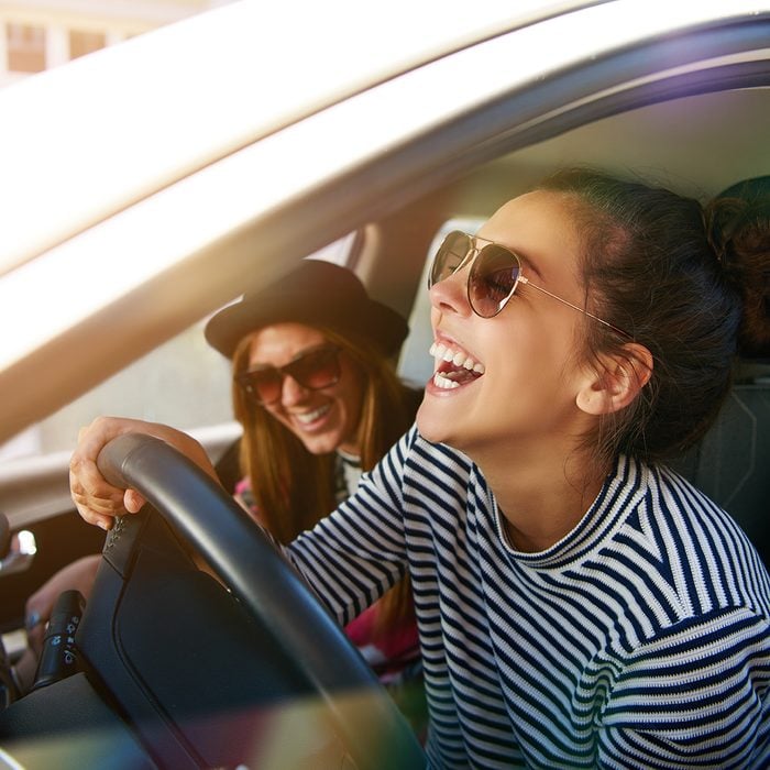Laughing young woman wearing sunglasses driving a car with her girl friend