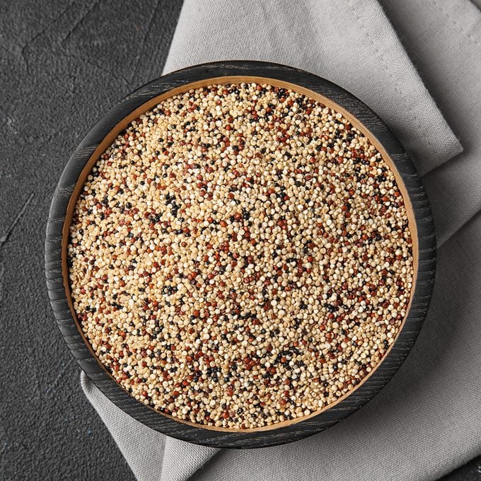 Plate with mixed quinoa seeds on dark background