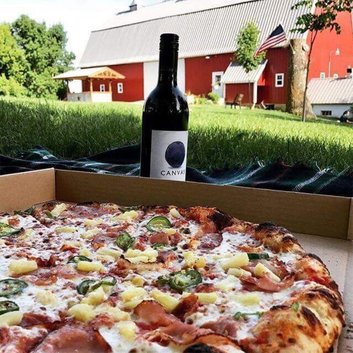 Red Barn Farm pizza and wine bottle on grass with a red barn in the background