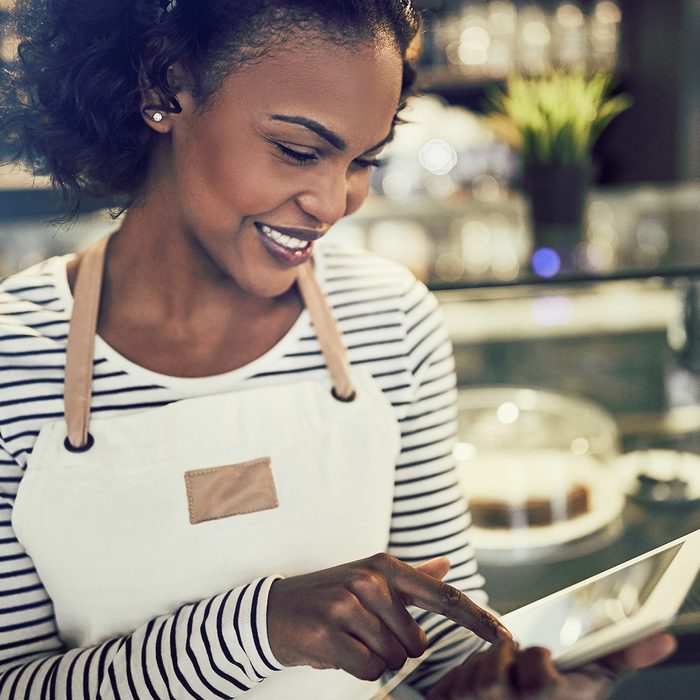 Smiling young African entrepreneur wearing an apron and using a digital tablet while standing in front of the counter of a trendy cafe ; Shutterstock ID 1059547061; Job (TFH, TOH, RD, BNB, CWM, CM): Taste of Home