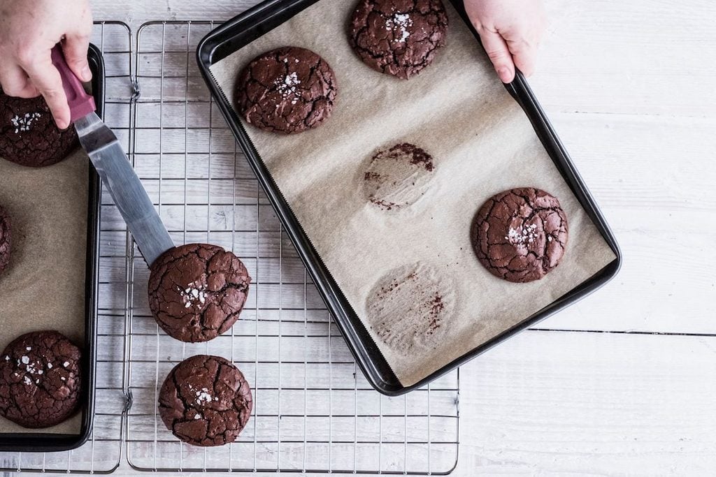 A person using a palette knife to move baked chocolate brownies from a baking tray to a cooling rack