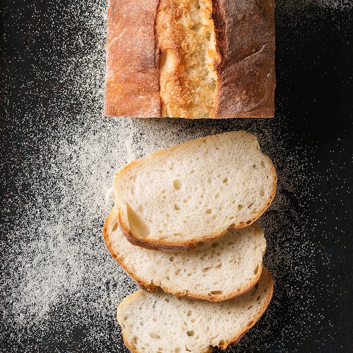 Sliced homemade white wheat bread with wheat flour on old black oven tray as background.