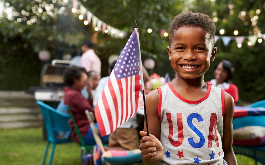 Young black boy holding flag at 4th July family garden party