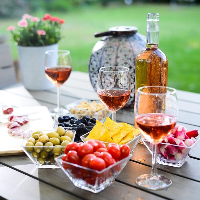 holiday summer brunch party table outdoor in a house backyard with appetizer, glass of rosé wine, fresh drink and organic vegetables