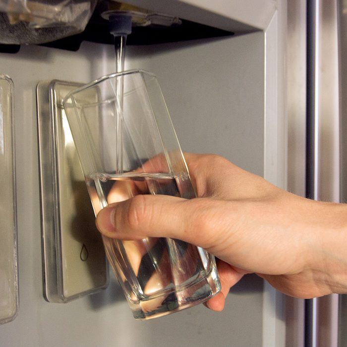 Male hand is pouring cold water from dispenser of home fridge.