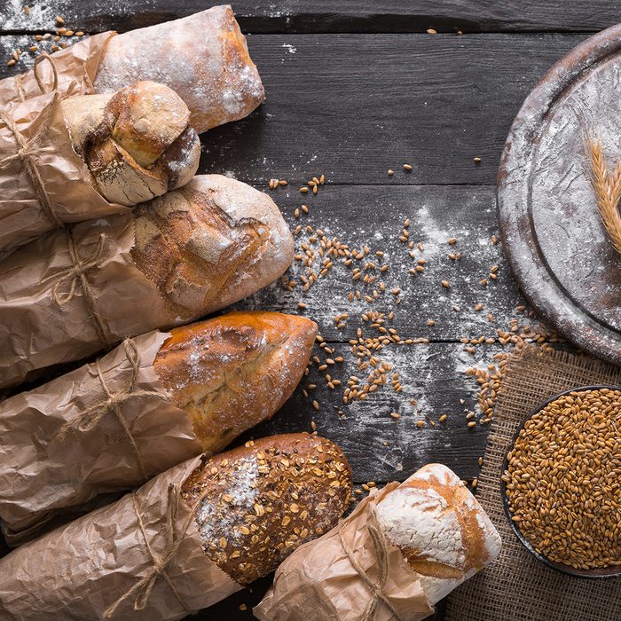 Bread background. Brown and white whole grain loaves wrapped in kraft paper composition on rustic dark wood