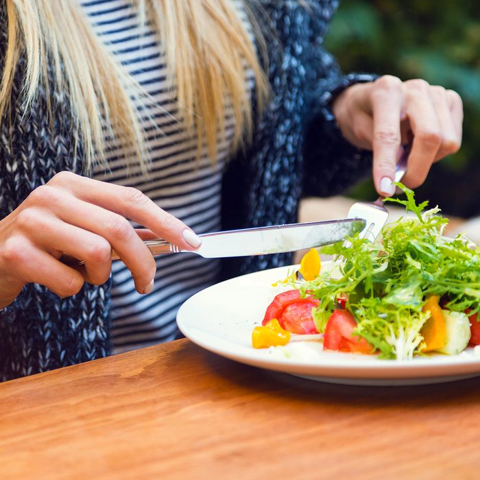 Blonde woman eating green healthy tasty eco salad on city street terrace