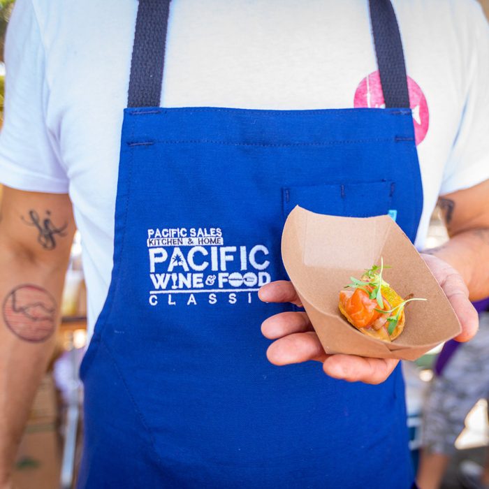 Pacific Wine and Food Classic man in blue apron holding snack in brown paper take out container