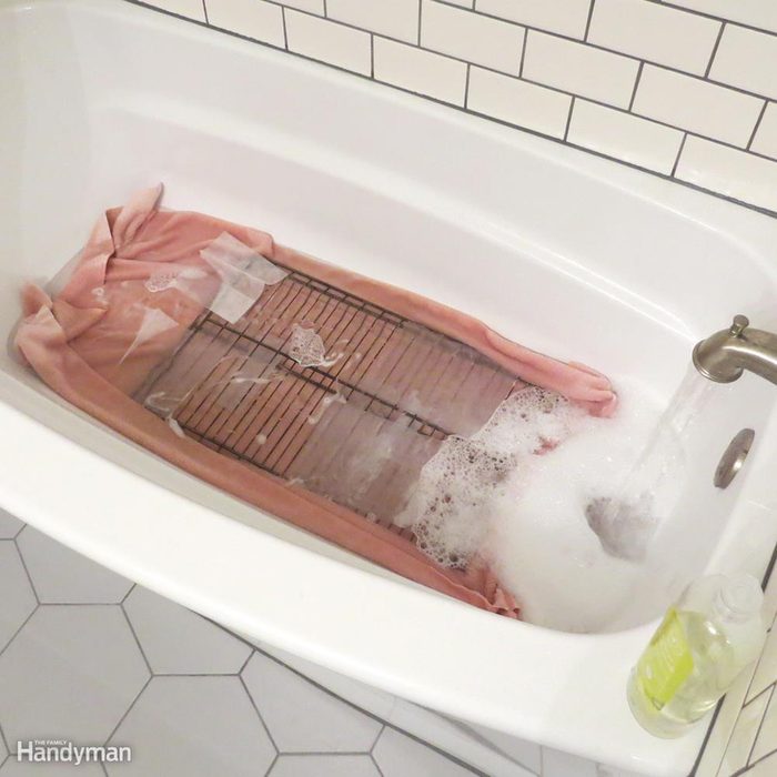Oven rack in bath tub submerged in water on pink towel