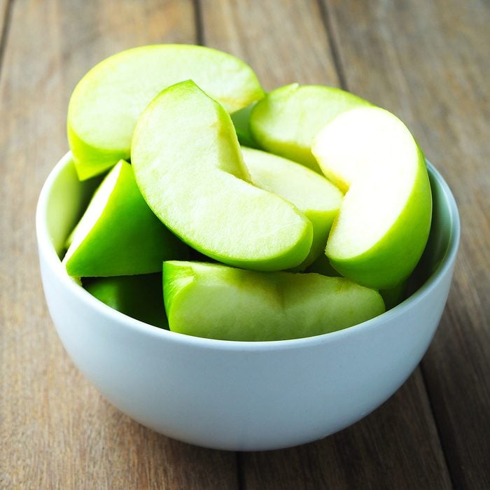 Close up of a bowl of apple slices on a wooden table.