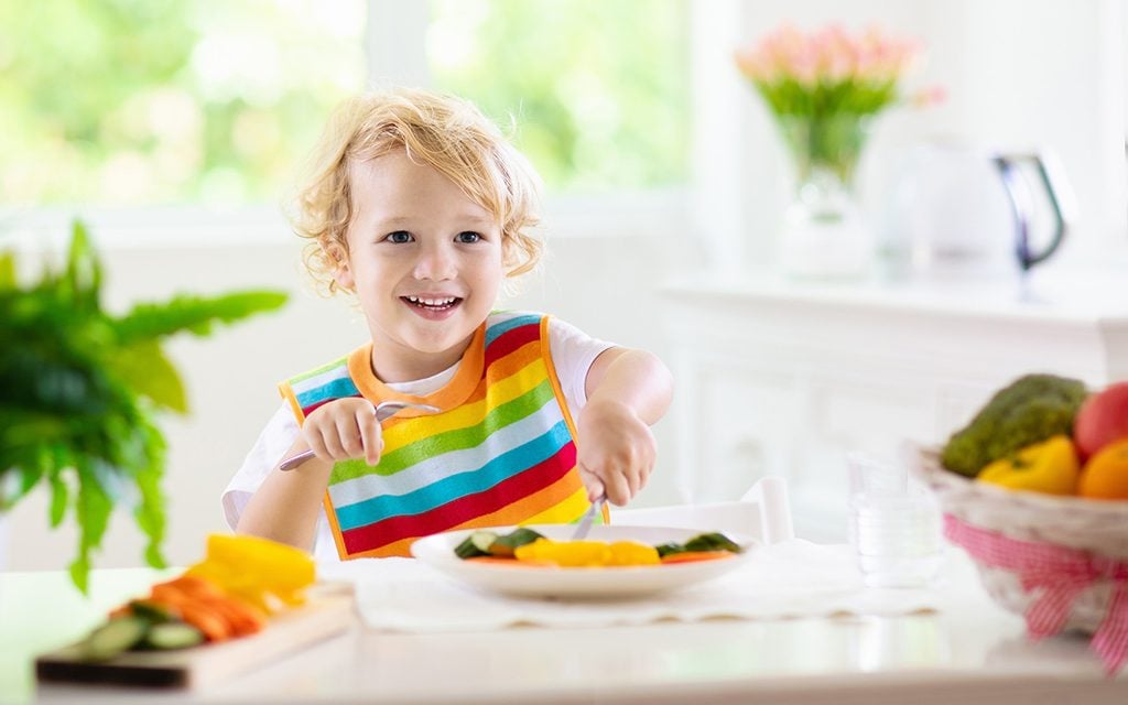 Child eating vegetables sitting in white high chair.