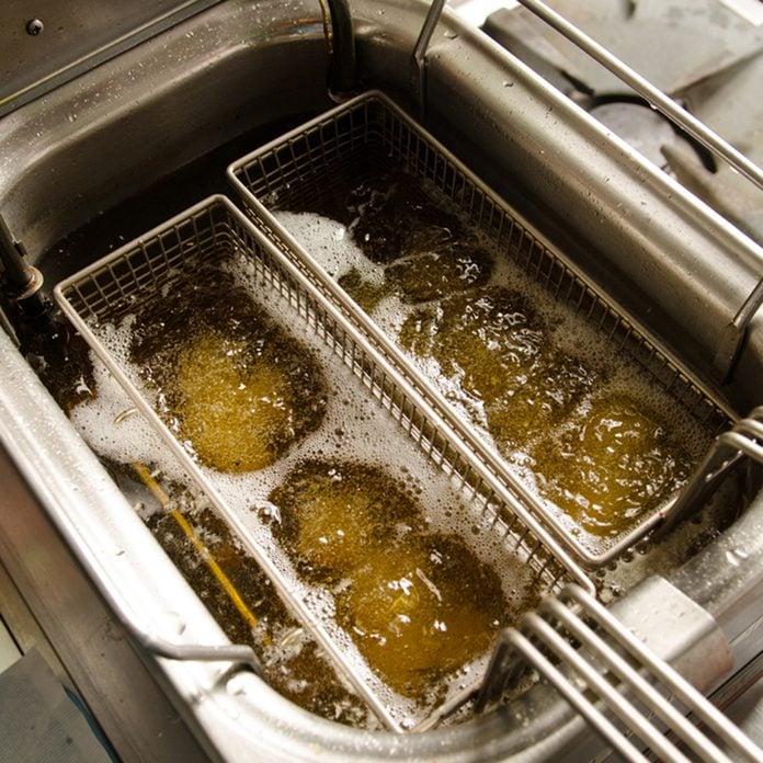 A deep pan industrial kitchen oil fryer, with golden oil, bubbling and frying potatoes