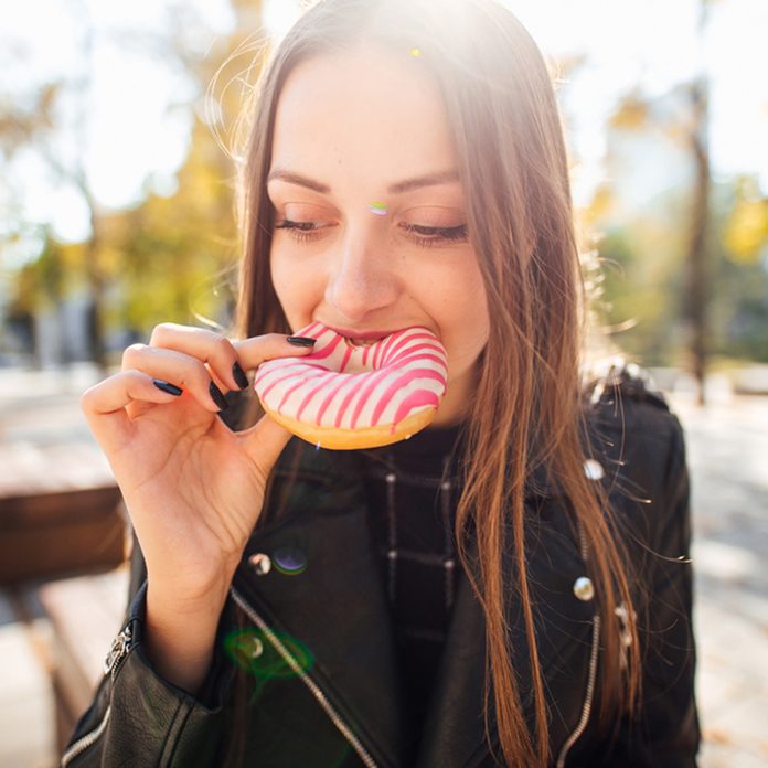 Young girl eat donut in park autumn background