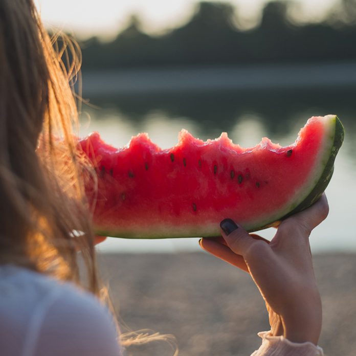 Girl eating watermelon and looking at the water.