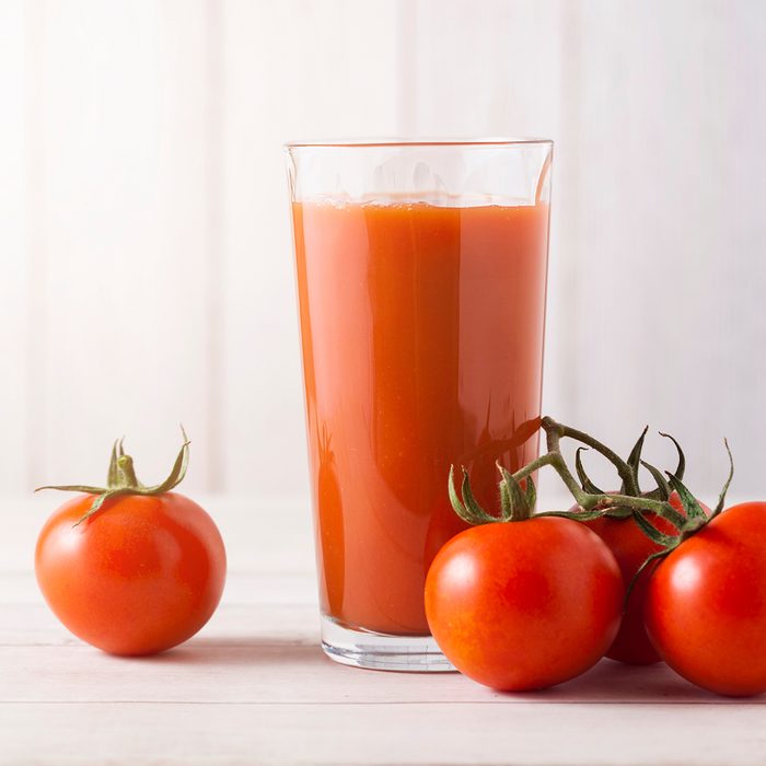 Glass of fresh organic tomato juice with raw tomatoes on light wooden background