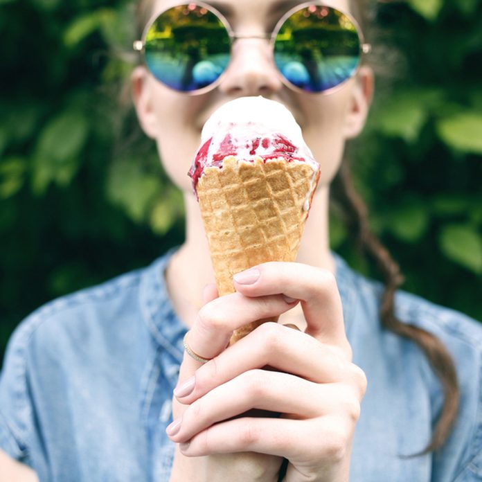 Outdoor closeup fashion portrait of young hipster crazy girl eating ice cream in summer hot weather in round mirror sunglasses have fun and good mood.