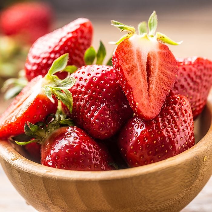 Juicy washed strawberries in wooden bowl on kitchen table.