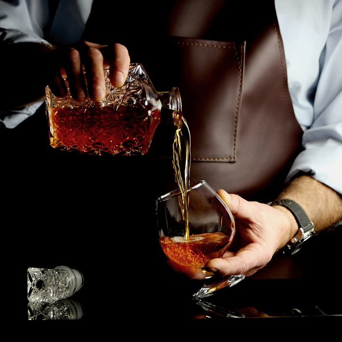 the man pours some brandy into a glass behind the bar