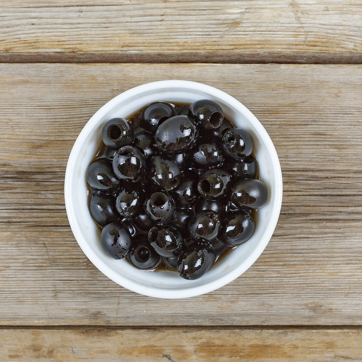 Olives in a white bowl on a wooden table, top view