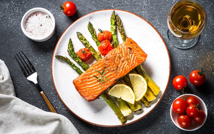 Baked salmon fish fillet with asparagus and tomato with glass wine on black stone table.