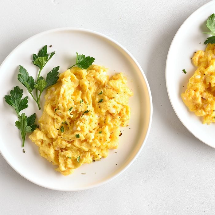 Scrambled eggs on plate over white stone background.