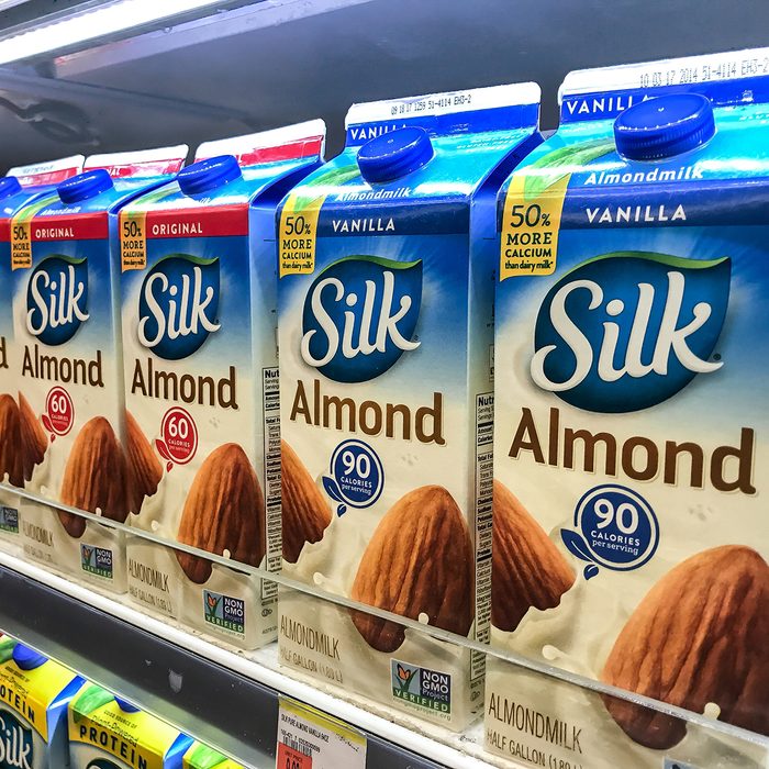 Cartons of almond milk stand on a shelf in a supermarket.