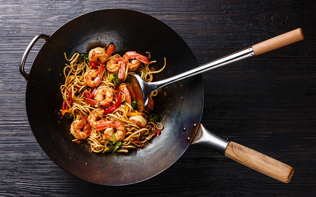 Udon stir-fry noodles with shrimp and vegetables in wok pan on black burned wooden background