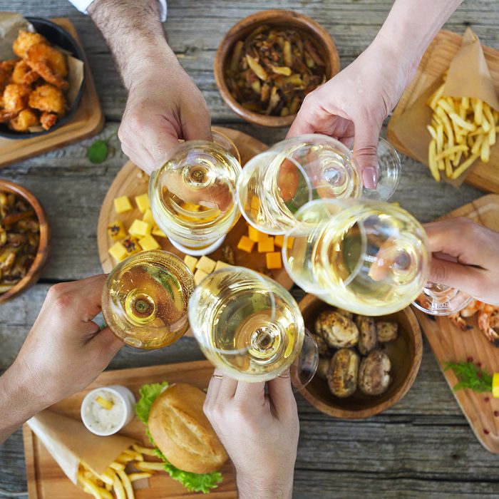 Hands with white wine toasting over served table with food.