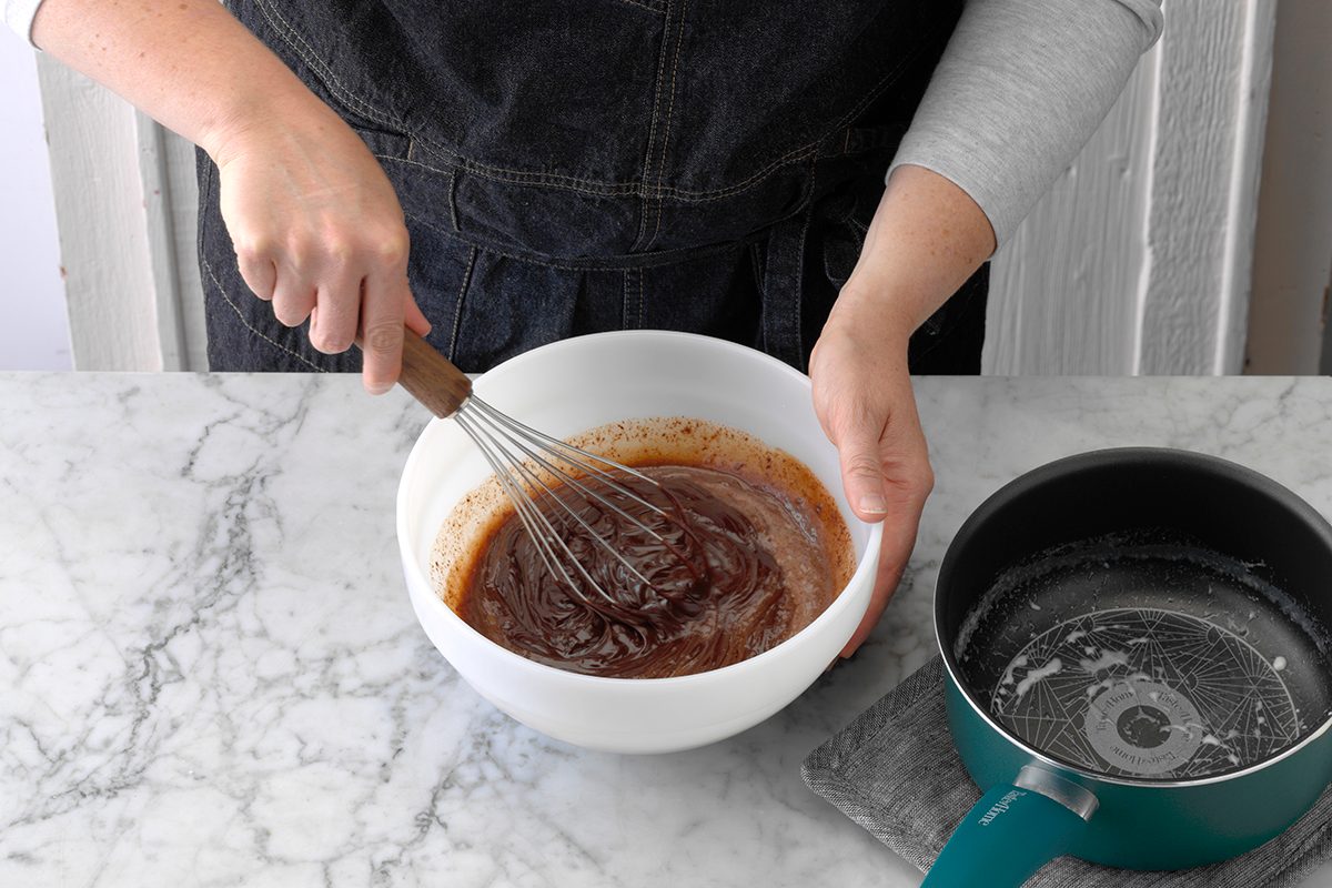 A person whisking chocolate chips and heavy whipping cream to make homemade chocolate ganache.