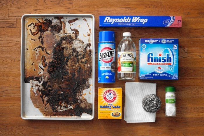 dirty baking sheet next to various cleaning supplies on a wood butcher block background