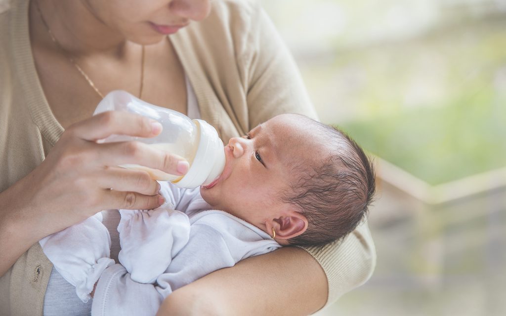 A portrait of cute newborn baby being fed by her mother using bottle