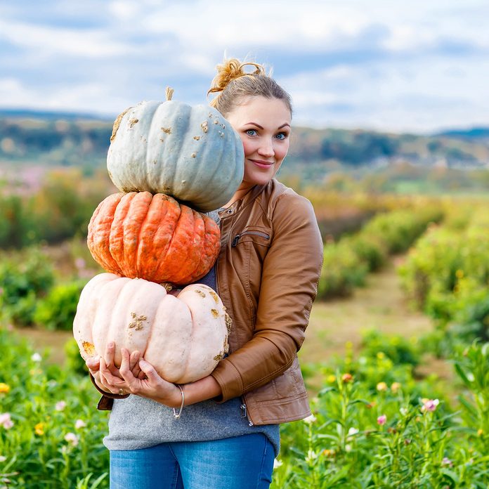Beautiful young woman with three huge different pumpkins on a farm or patch.