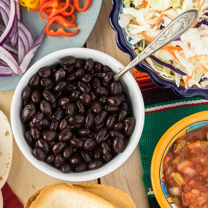 Top view of bowl with black beans, mini taco boats, cabbage, salsa - ingredients for taco with black beans and vegetables.