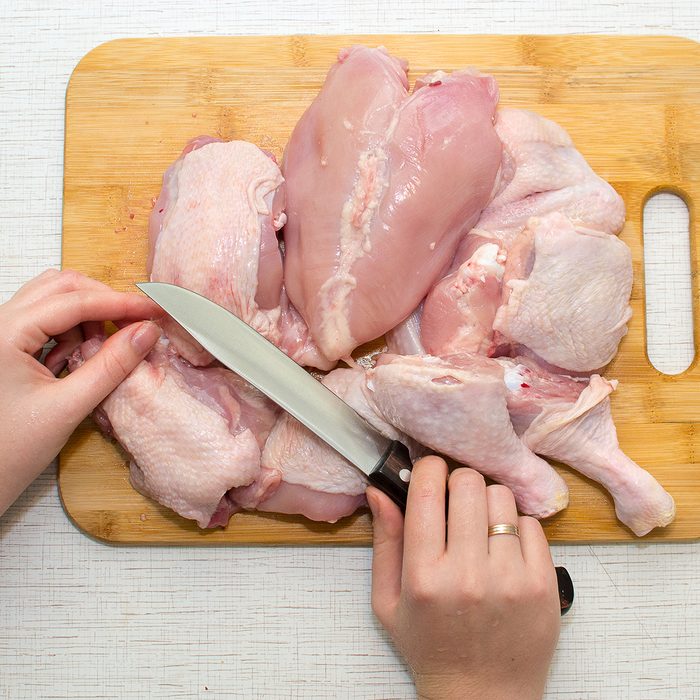 Chef woman carves a whole chicken carcass on a wooden Board