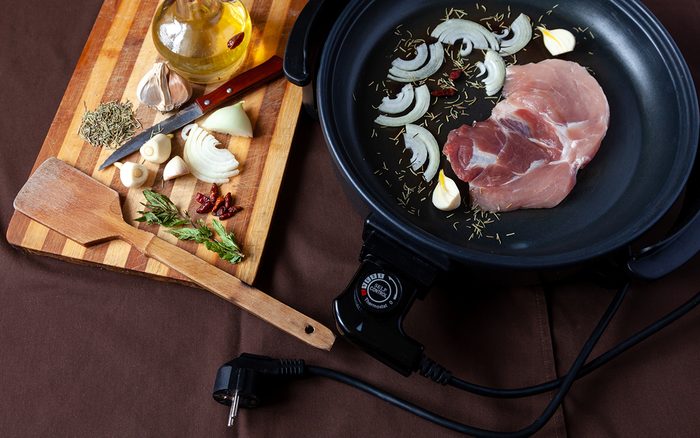Electric pan with meat of pork on the table. Independent auxiliary skillet for cooking any place.