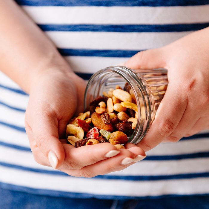 Hands holding a jar of nuts and dried fruits.
