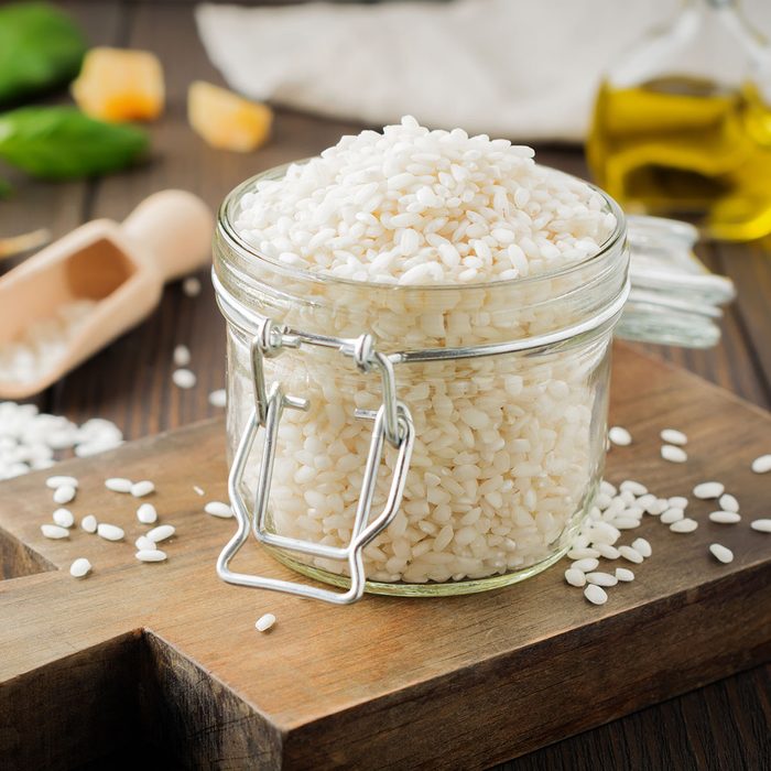 Raw White rice variety Arborio for Italian risotto dishes in glass jar on dark wooden background.