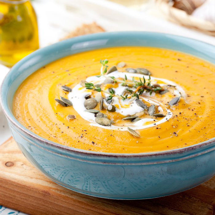 Roasted pumpkin and carrot soup with cream and pumpkin seeds on white wooden background.