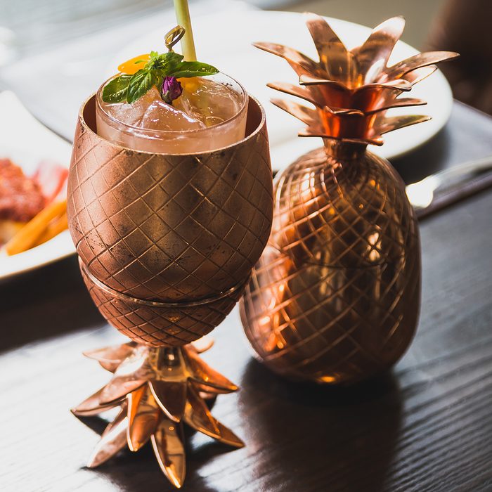 Cocktail served inside copper pineapple cup with dishes in the background. ; Shutterstock ID 1080759941; Job (TFH, TOH, RD, BNB, CWM, CM): TOH
