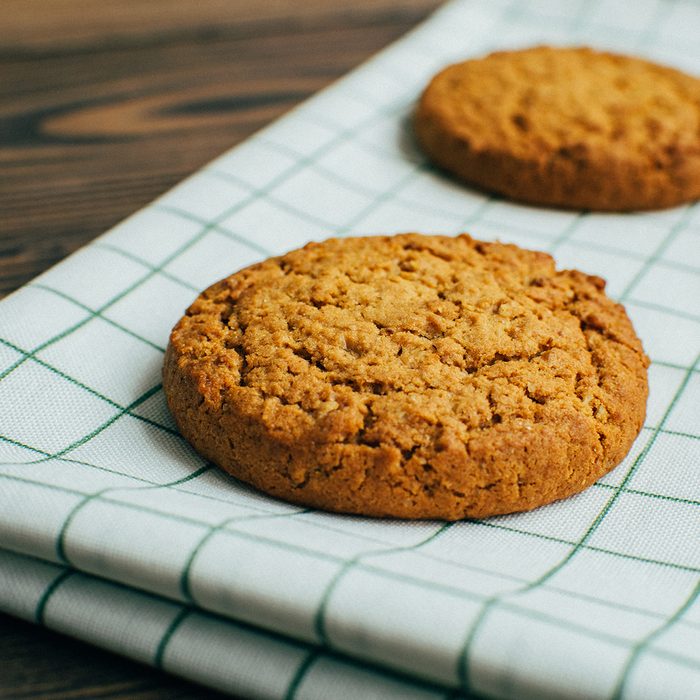 Close-up three tasty oatmeal cookies laying at the green checkered textile kitchen towel at wooden surface of bakery, cafe or kitchen table in the morning during the breakfest in cozy atmosphere