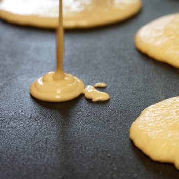Pancake batter baking mix being poured from a bowl onto a hot electric griddle cooking delicious breakfast meal for a family.; Shutterstock ID 482260003; Job (TFH, TOH, RD, BNB, CWM, CM): Taste of Home