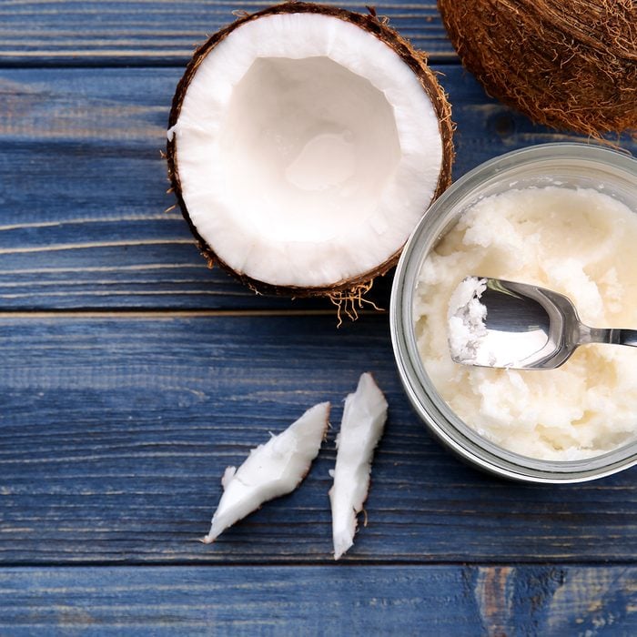 Opened glass jar with fresh coconut oil on wooden background