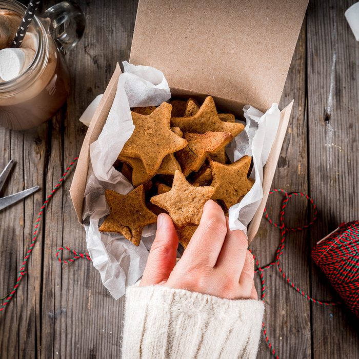 Traditional autumn winter drinks and treats. Cup of hot chocolate with marshmallow and ginger biscuit stars, in gift box, old rustic wooden table. Person takes cookies from box, top view copy space; Shutterstock ID 694951078; Job (TFH, TOH, RD, BNB, CWM, CM): Taste of Home